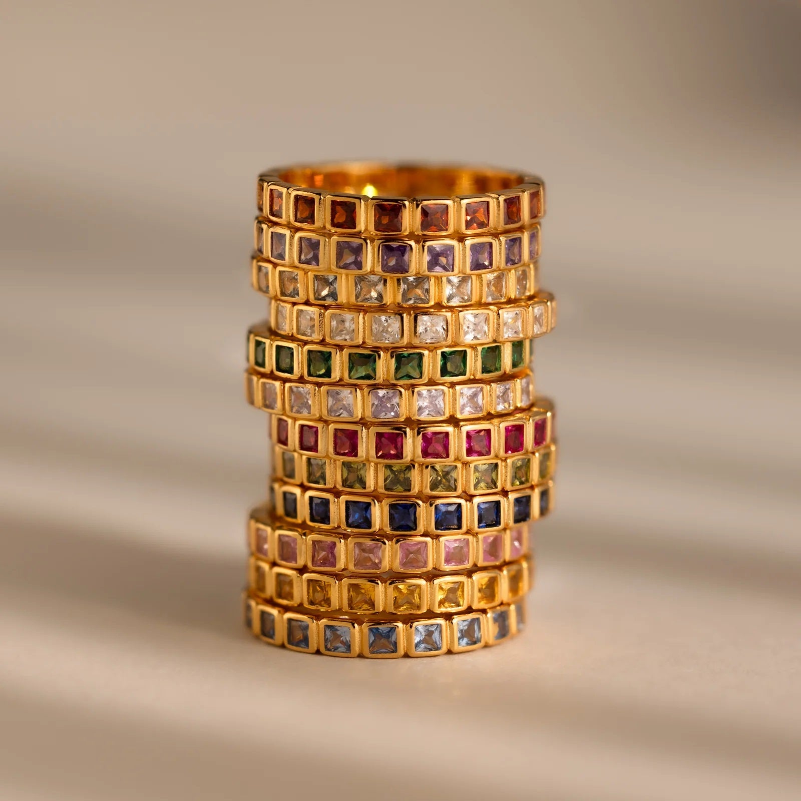 Stack of gold rings with gemstones on a beige background